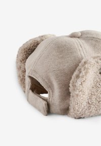 Lys beige kasket med bløde øreklapper. Fremstillet af blødt stof, med en rund form og justerbar rem bagpå.