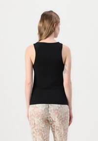 Haut sans manches noir avec un décolleté rond et un design ajusté, associé à un pantalon en dentelle crème comportant des motifs floraux complexes.