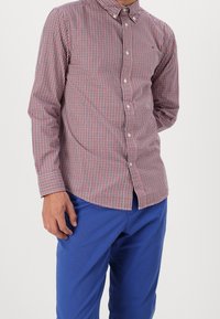 Red and blue checked button-up shirt with a collar, featuring long sleeves and a curved hem, paired with solid blue pants.