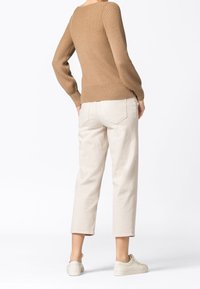 Beige Rippenpullover mit schmalen Bündchen, kombiniert mit cremefarbenen, schmal zulaufenden Hosen und hellen Sneakers. Glatte Texturen, minimale Details.