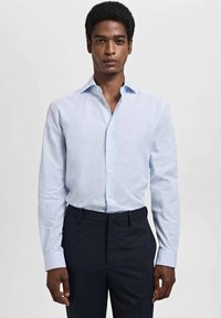 Lichtblauw gestreept dresshirt met een klassieke kraag en lange mouwen, gecombineerd met donkere broek. De stof ziet er soepel en op maat gemaakt uit.