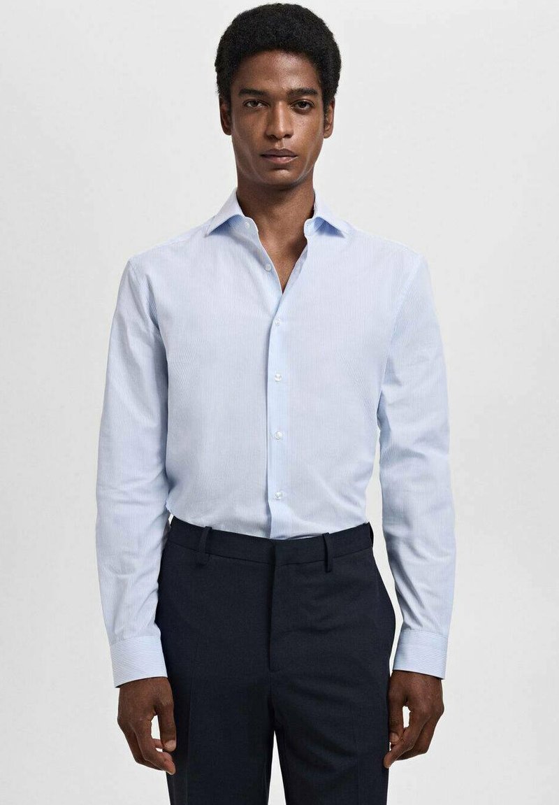 Lichtblauw gestreept dresshirt met een klassieke kraag en lange mouwen, gecombineerd met donkere broek. De stof ziet er soepel en op maat gemaakt uit.