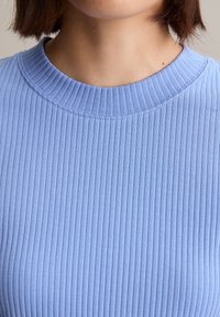 Top de punto acanalado azul claro con cuello redondo. La tela presenta surcos verticales, proporcionando textura y un aspecto ajustado.