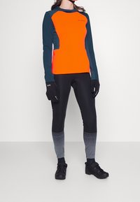 Orange och teal långärmad topp kombinerad med svarta leggings med ett gradient mönster i grått. Svarta handskar och vandringsskor fulländar looken.