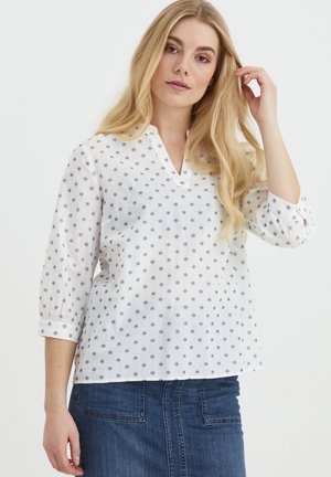 Weißes Blusenshirt mit V-Ausschnitt, dreiviertel Ärmeln und einem dezenten marineblauen Blumenmuster. Leichtes, strukturiertes Material, kombiniert mit einem Jeansrock.