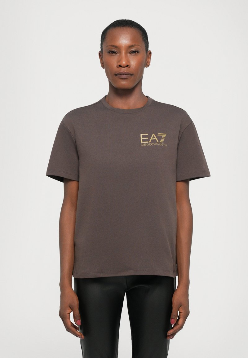 Brun bomull t-skjorte med korte ermer og rund hals. Har en gull EA7 Emporio Armani-logo på brystet. Glatt tekstur.