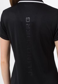 Černé polokošile z lehké tkaniny. Má bílý pruhovaný límec a vertikální logo na zádech s matným povrchem.