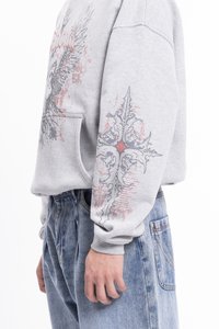 Szary sweatshirt z przednią kieszenią, z szczegółowymi grafikami skrzydeł i ozdobnym krzyżem w czerni i czerwieni na rękawach. Luźny krój.