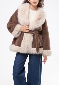 Cappotto in pelliccia sintetica marrone e beige con ampio colletto, una cintura e una consistenza morbida. Presenta sezioni di colore a contrasto e polsini soffici.