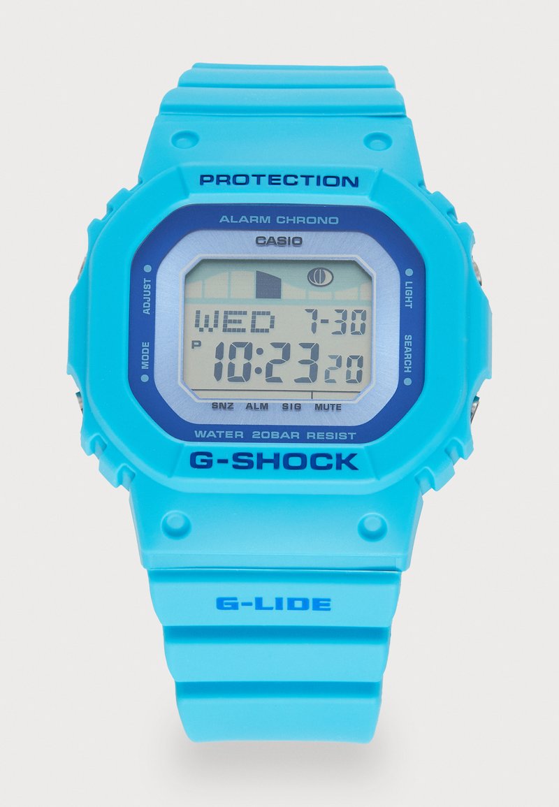 Cyfrowy zegarek Casio G-Shock w jaskrawym niebieskim kolorze z kwadratową tarczą, z szarym wyświetlaczem pokazującym czas i dzień oraz tekstylnym paskiem z silikonu.