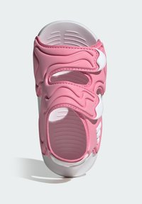 Różowe sandały z gumopodobną górą ozdobioną falistymi wzorami, dwoma regulowanymi białymi paskami, teksturowaną wkładką oraz białą podeszwą.