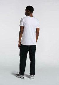 T-shirt bianco a maniche corte con colletto rotondo, abbinato a pantaloni cargo neri. L'outfit presenta una vestibilità rilassata e tasche pratiche.