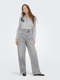 Camicia a righe bianca e nera con ricami floreali, abbinata a jeans grigi chiari a vita alta e a gamba larga. Scarpe basse nere.