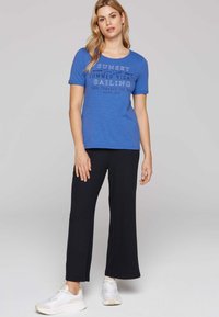 Camiseta azul de manga corta con texto de temática náutica, combinada con pantalones anchos de canalé negros y zapatillas blancas. Conjunto simple y casual.