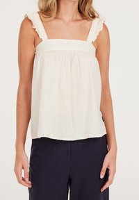 Biały, teksturowany top bez rękawów z kwadratowym dekoltem i falbaniastymi ramiączkami. Luźny fason, zestawiony z ciemnymi spodniami.