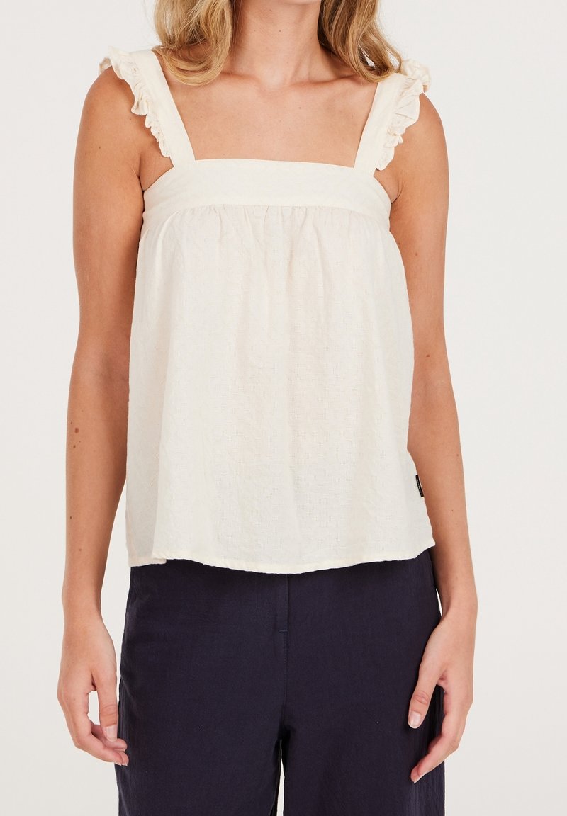 Biały, teksturowany top bez rękawów z kwadratowym dekoltem i falbaniastymi ramiączkami. Luźny fason, zestawiony z ciemnymi spodniami.