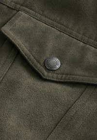 Olive green suede fabric with a light texture, featuring a flap with a silver snap button marked "Premium Grade Durable Goods."