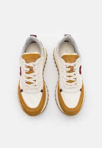 Tenisky s bílým koženým svrškem, béžovými semišovými akcenty a šedou textilní podšívkou. Mají béžové tkaničky a hnědou gumovou podrážku.