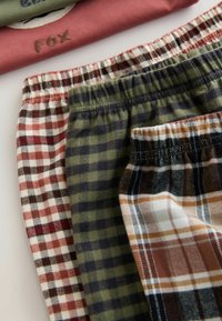 Četras pāra rakstainu pleda šortu ar dažādām krāsām: sarkani un balti, zaļi un melni, brūni un krēmīgi, un zili un brūni, ar elastīgām jostasvietām.