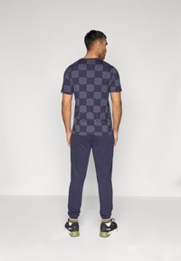 Camiseta de color azul marino con estampado de cuadros. Combinada con joggers azul marino a juego y zapatillas deportivas negras con suelas verdes.