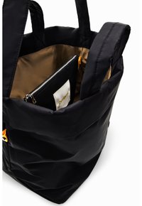 Svart tote bag med vadderad utsida, gyllene detaljer och brunt foder invändigt. Inkluderar en zippered svart väska med en etikett.