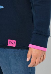 Felpa blu navy con dettagli sui polsini in rosa e un'etichetta rosa con simbolo dell'infinito. Il materiale sembra morbido e presenta un design casual.