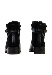 Bottines noires en suède et cuir synthétique. Elles présentent un petit talon, une boucle décorative et des sangles croisées à l'arrière.