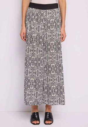 Donna che indossa pantaloni a gamba larga con motivo bianco e nero, con vita elastica nera e zoccoli neri intrecciati con tacco e punta aperta.