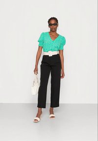 Blusa verde de bolinhas com mangas curtas bufantes, cinto branco, calças pretas e mala branca. Usada com sandálias chunky bege.