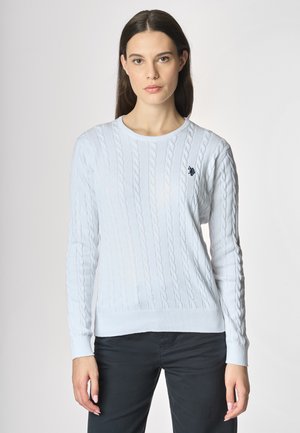 Maglione azzurro chiaro a maglia rasata con scollo rotondo e polsini a costine, decorato con un piccolo emblema scuro sul lato sinistro del petto.