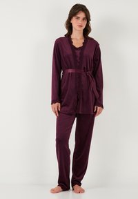 Paars satijnen loungewear-set bestaande uit een lange mouwen jasje met kantafwerking, bijpassende broek en een strikceintuur. Zachte textuur en ontspannen pasvorm.