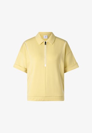 Polo w jasnawożółtym kolorze z krótkim rękawem, zamkiem błyskawicznym z przodu, podwiniętymi mankietami i białą lamówką wzdłuż szwów na białym tle.