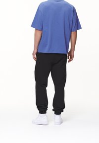 Camisa azul de manga corta y pantalones de chándal negros con puños elásticos ajustados. Zapatillas blancas visibles, textura de tela suave en toda la prenda.