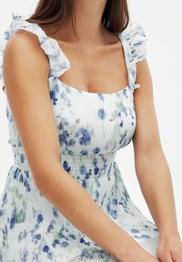Robe florale avec des motifs bleus et verts sur un fond clair, dotée de bretelles froncées et d'une taille smockée.
