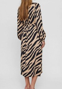 Langes, beiges Kleid mit schwarzen Zebra-Streifen, ausgestattet mit einem taillierten Bund, langen Ärmeln und einer Midi-Länge bis zur Wade. Weicher Stoff sichtbar.