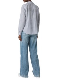 Gestreiften Hemd in Blau und Weiß, mit abgerundetem Saum und langen Ärmeln. Kombiniert mit locker sitzenden hellblauen Jeans.