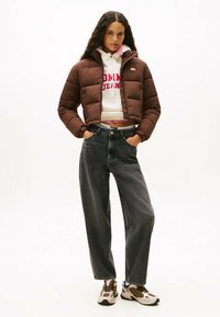 Giubbotto puffo marrone, felpa bianca con testo rosso, jeans neri a vita alta e sneakers marroni con dettagli in rete. Estetica casual streetwear.