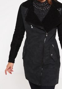 Cappotto in finta suede nero con un ampio colletto, zipper frontali, tasche laterali e tessuto testurizzato. Presenta un design di lunghezza intermedia e materiali a contrasto.