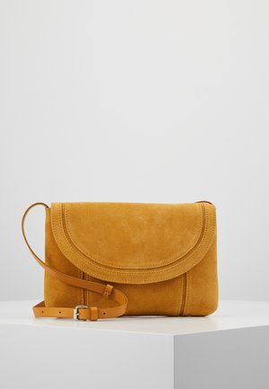 Sennepsgul ruskind crossbody taske med flaplukning og justerbar tynd læderrem på en hvid overflade mod en ensfarvet baggrund.