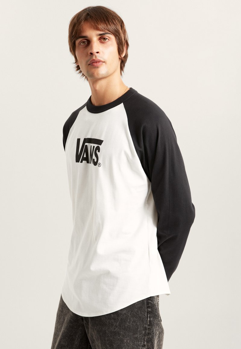 T-shirt à manches longues en raglan blanc et noir, avec un grand logo "VANS" noir sur le devant et des couleurs de manches contrastées. Tissu en mélange de coton.