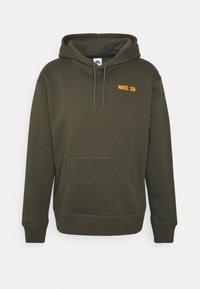 Tmavě zelená kapuce Nike SB s přední kapsou, stahovací kapucí a oranžovým logem na levé straně hrudi. Měkká tkanina, klasický design přes hlavu.