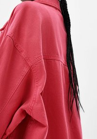 Lekka, luźna czerwona koszula z denimu z kołnierzykiem i widocznym detalem przeszycia, prezentująca teksturowany materiał.