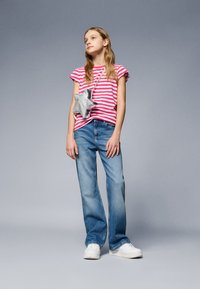 T-shirt riscada em rosa e branco com mangas viradas, jeans azuis de perna larga e ténis brancos. O conjunto é complementado com uma bolsa prateada em forma de estrela.