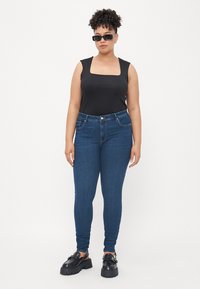 Black sleeveless top, blue skinny jeans, and black platform shoes. The top has a square neckline. Textured denim with a smooth finish.