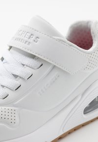 Witte sneaker met geperforeerde accenten, bovenzijde van textiel, gevoerde kraag en verstelbare band. Beschikt over een transparante luchtkussen en rubberen loopzool.