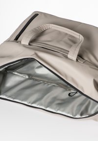 Beige Tasche mit einer glatten, matten Oberfläche, ausgestattet mit einem oberen Reißverschluss, einer kleinen Außentasche und einem silbernen Innenfutter. Die Griffe sind in das Design integriert.
