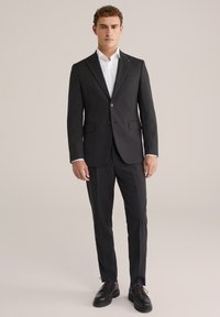 Melnā uzvalkā ar vienrindu žaketi, ar griezumu pie apkakles un divām priekšējām kabatām. Apvienots ar baltu kreklu un melniem lakotiem apaviem.