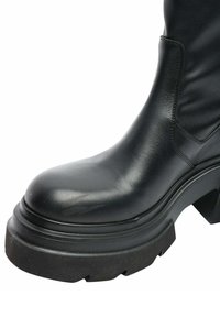 Stivale alla caviglia in pelle nera con punta arrotondata, suola in gomma nera spessa con finitura testurizzata e dettagli di cucitura laterale.