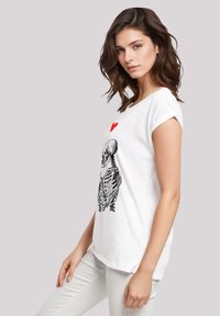 Weißes Baumwoll-T-Shirt mit einem schwarzen Skelett-Graphic und einem roten Herz, lockere Passform, kurze Ärmel und rundem Ausschnitt.
