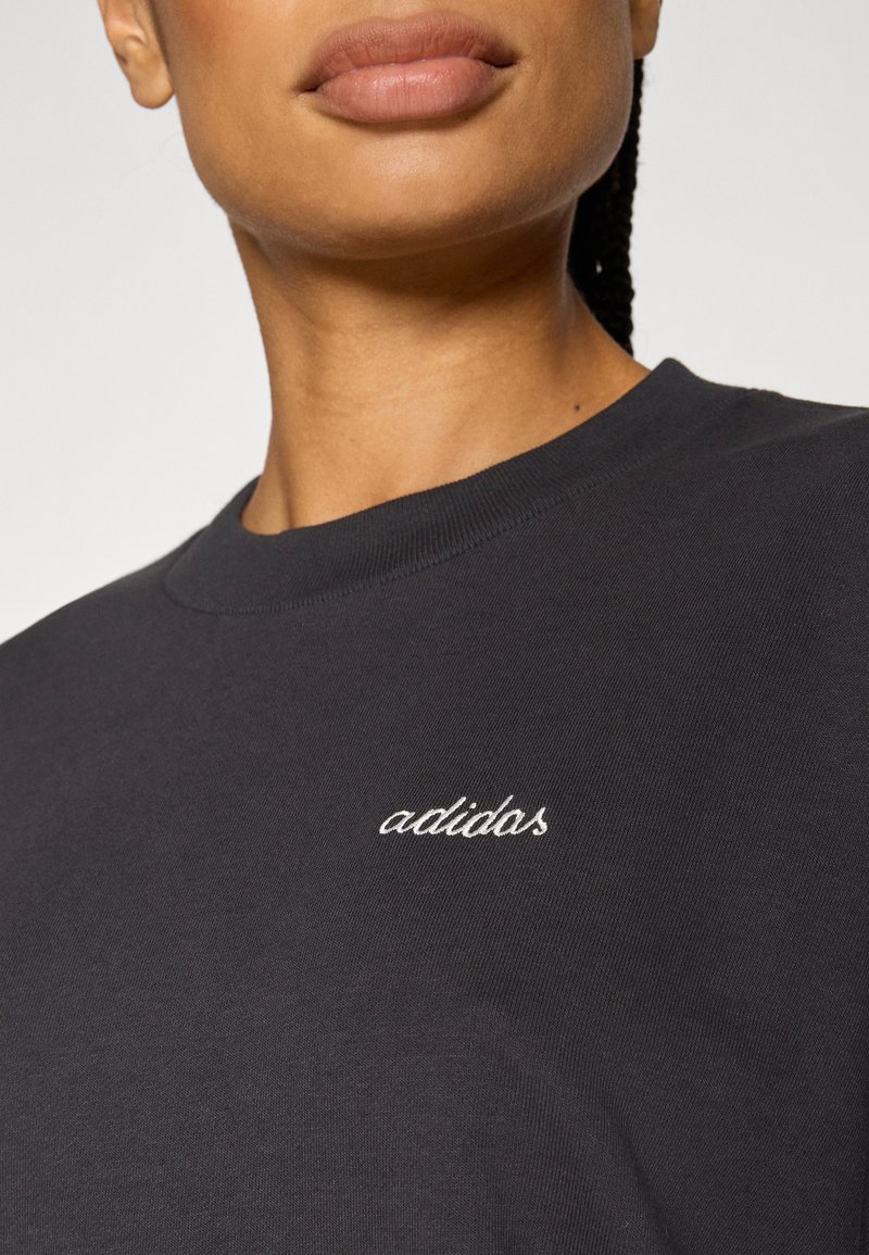 Sweat-shirt noir à col rond, avec une broderie cursive blanche "adidos" sur la poitrine. Confectionné en tissu doux et texturé.